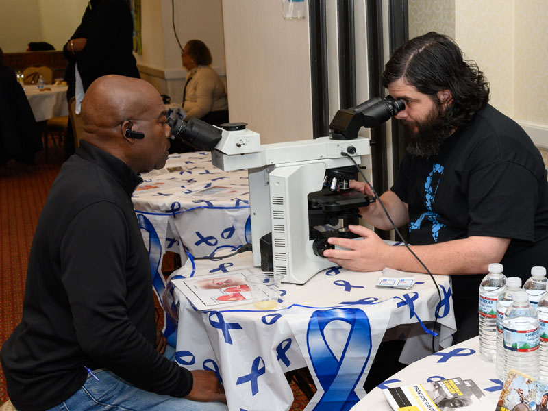 Dr. Greg Dickinson and attendee with double-headed microscope, Men’s Prostate Cancer screening event, Mount Vernon, NY, fall 2019.